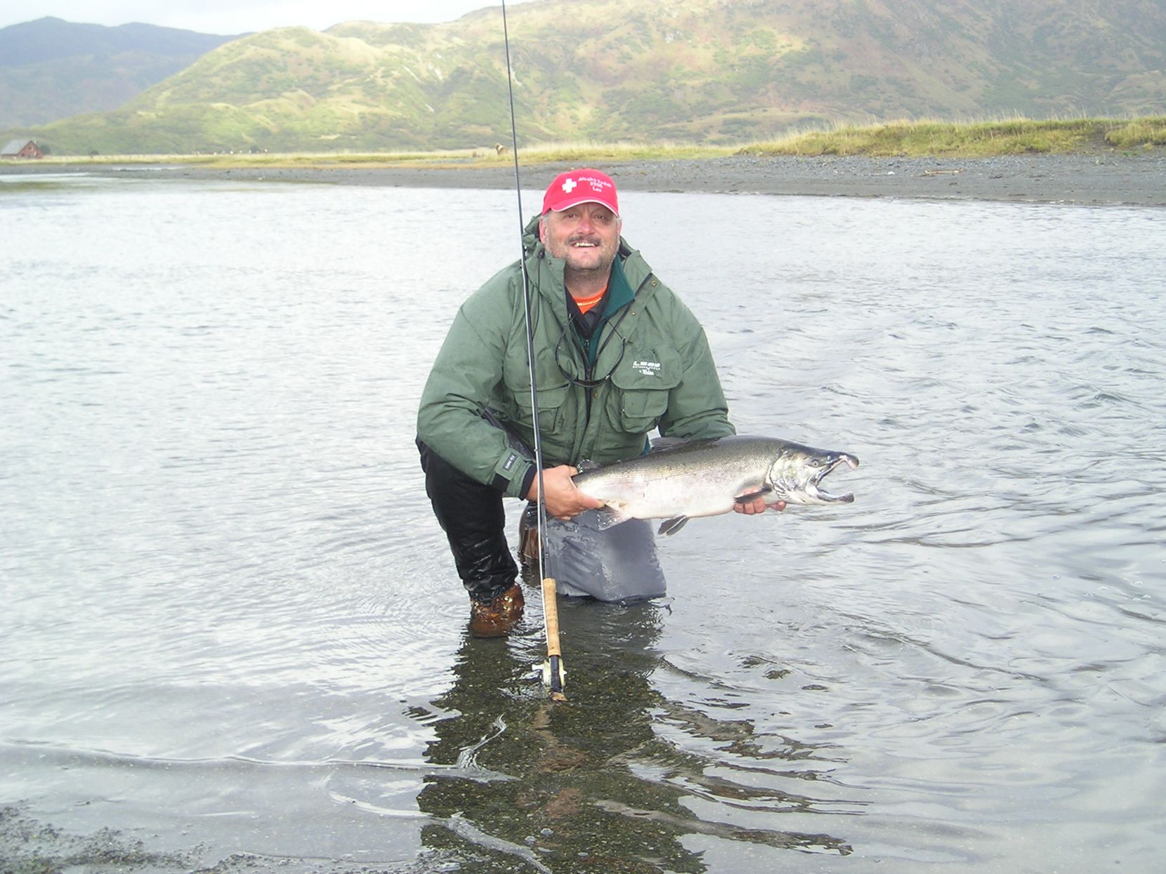 Mann steht im Fluss mit Fliegenfischerrute und Fisch.